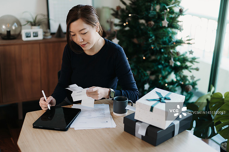 管理个人银行和财务的年轻亚洲女性，在圣诞节购物后在家中整理各种费用收据，用数位板规划预算和计算支出，家庭财务，假日期间的家庭预算图片素材