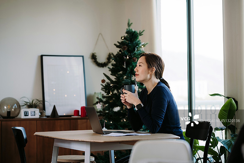 圣诞节期间使用笔记本电脑的亚洲年轻女性。上网和在线进行圣诞节购物。家里装饰着圣诞树和装饰品。圣诞节生活方式。圣诞节购物。电子商务，非接触式支付。节日和喜庆氛围图片素材