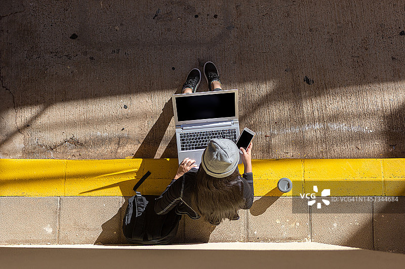 学生坐在阳光明媚的街道上使用电脑和手机图片素材