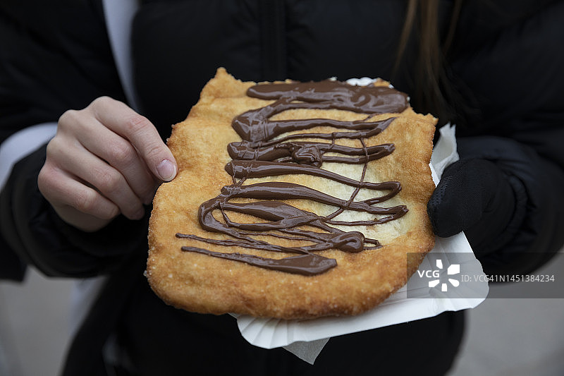 青少年拿着淋有融化巧克力的炸面包，在德国圣诞市场购买的街头小吃图片素材