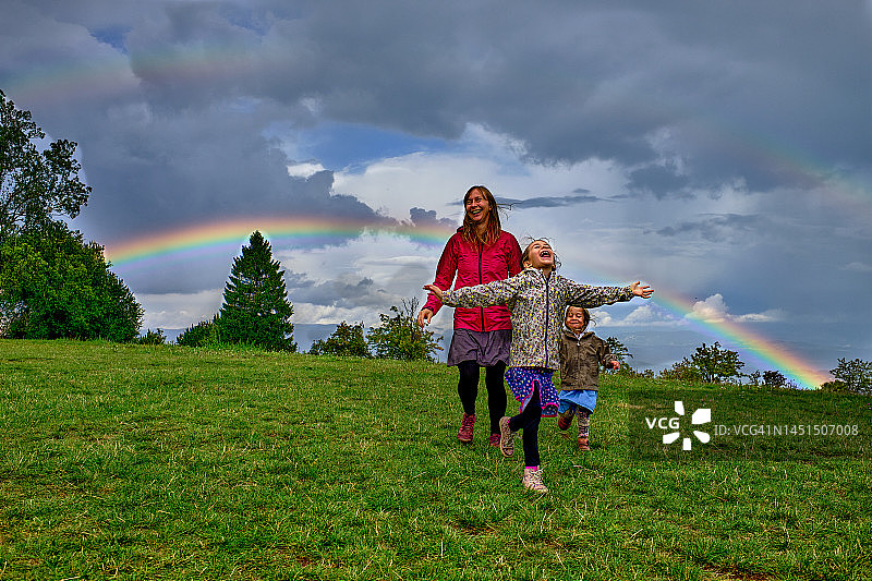 年轻母亲和两个女儿在彩虹下奔跑图片素材
