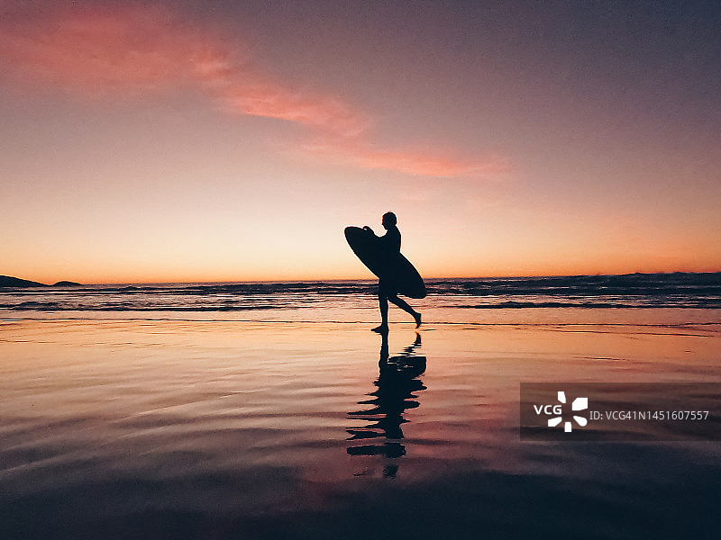 冲浪者在日出时分于海滩上行走图片素材