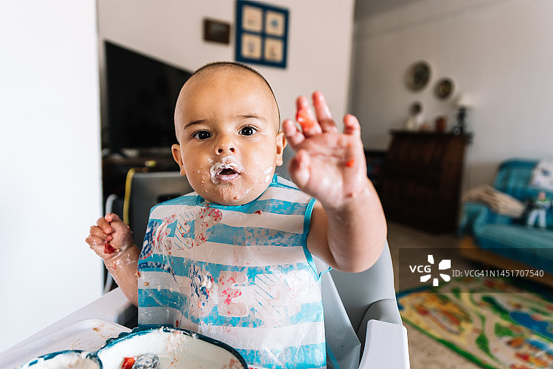系着围嘴的宝宝自己吃饭，坐在高脚椅上，宝宝主导的断奶方法图片素材