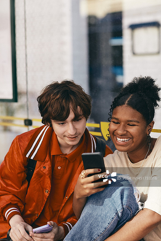 看快乐少女拿着的智能手机的年轻男人图片素材