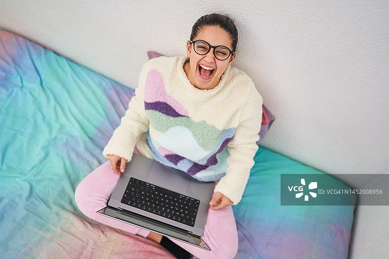 快乐的年轻女子戴着眼镜在床上使用笔记本电脑图片素材