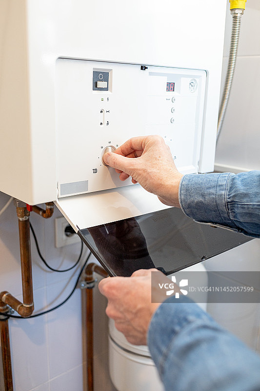 由于能源危机，白人男子降低家中燃气锅炉的温度图片素材