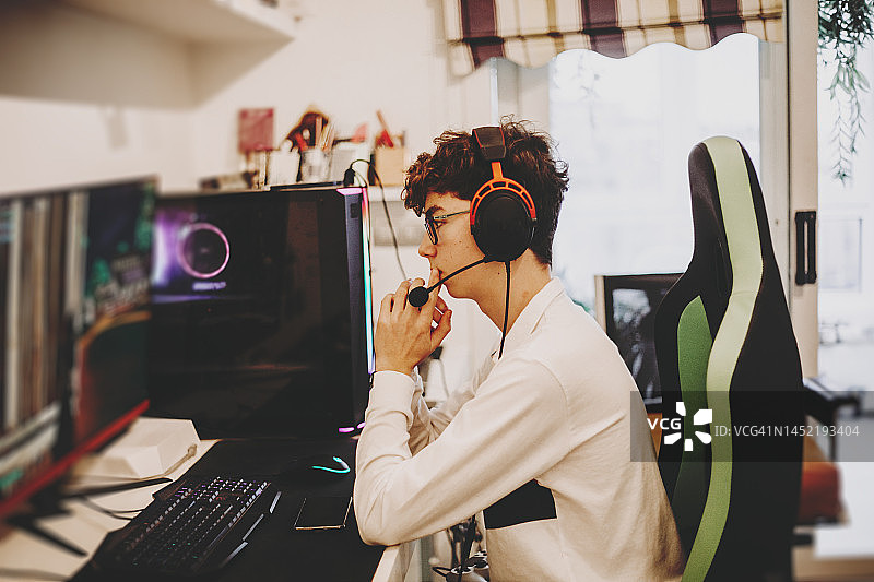 戴着耳机的青少年男孩玩电脑游戏的特写图片素材