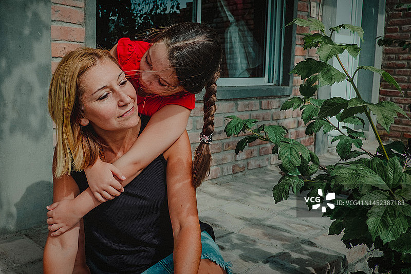 7岁女孩从背后拥抱年轻的金发母亲图片素材