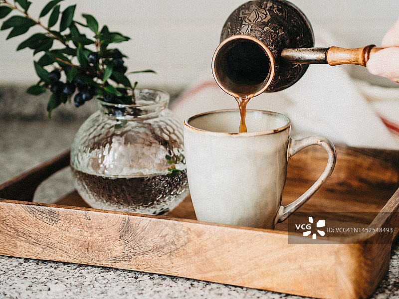 女人将热咖啡从土耳其咖啡壶倒入杯中图片素材