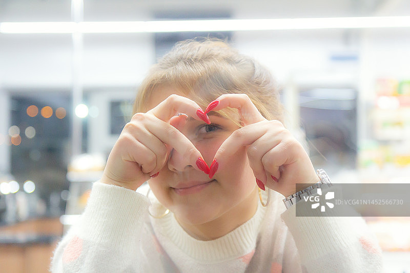 用手比心——恋爱中的年轻女子坐在咖啡馆里，透过爱的手势看图片素材