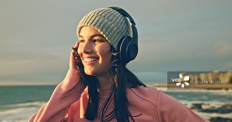 在海滩上戴着耳机听音乐的快乐女人图片素材