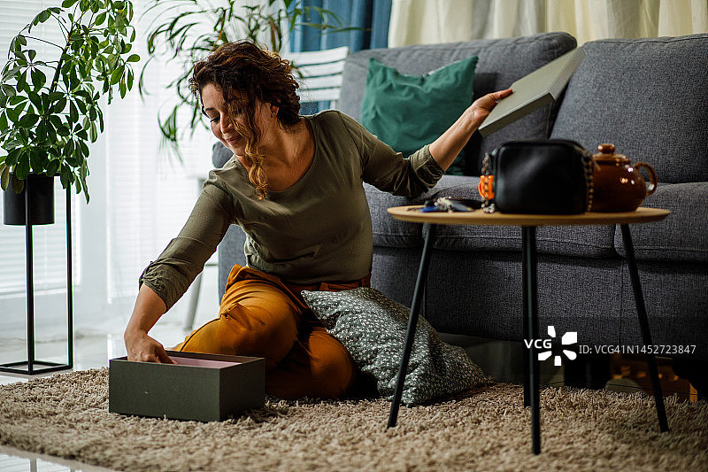 坐在客厅地板上打开包裹的快乐女人的肖像图片素材