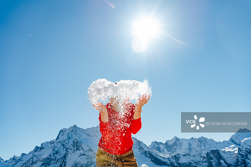 穿红色毛衣的女人在阳光明媚的山区里扬起雪堆图片素材