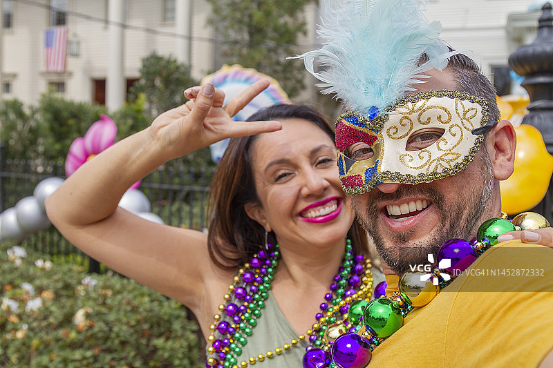 快乐的拉丁游客朋友/异性恋夫妇在新奥尔良庆祝狂欢节，戴着项链和面具自拍。图片素材