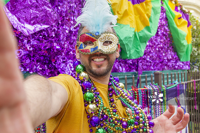 一位戴着面具、穿着服装、戴着项链的拉丁裔年轻游客在庆祝新奥尔良的狂欢节时，用手机自拍。图片素材