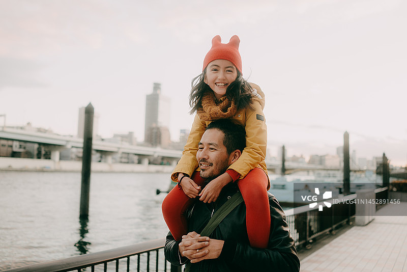 冬天，父亲在东京的城市河流边让女儿骑在肩上图片素材