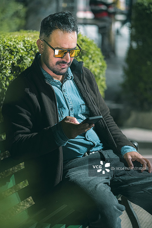 单身男人坐在公园长椅上使用智能手机图片素材