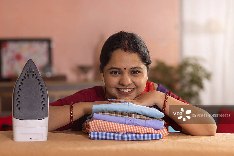 看着镜头，下巴靠在熨烫衬衫上的快乐女人特写图片素材