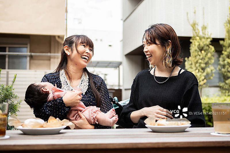 母亲抱着两个月大的女儿在咖啡馆的开放空间享用午餐，还有她即将分娩的怀孕朋友图片素材