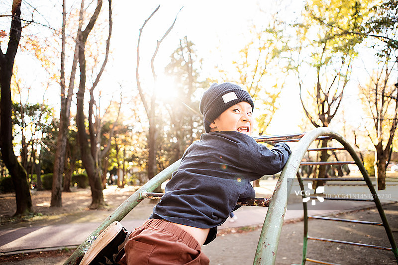 男孩在公园的单杠上做鬼脸玩耍图片素材