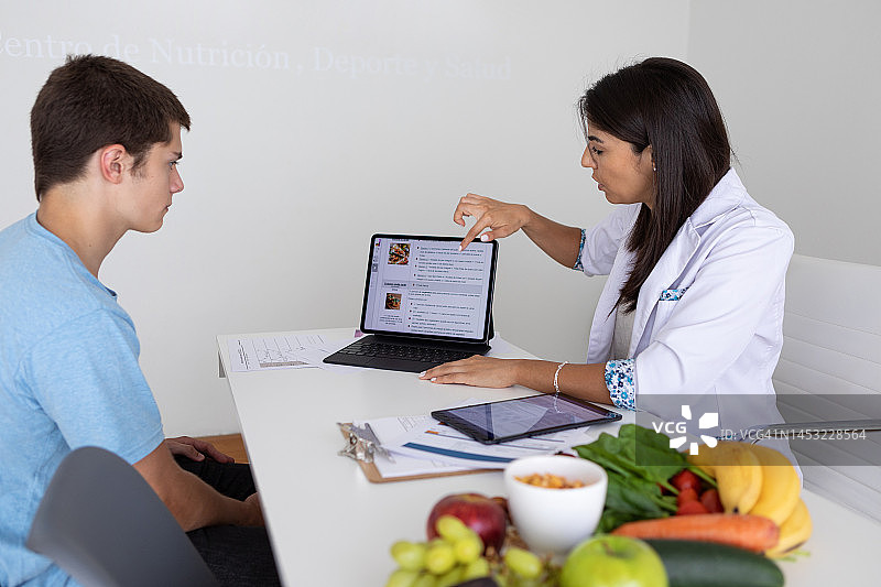 女营养师医生和运动生理学家在办公室为青少年男患者进行医疗咨询图片素材
