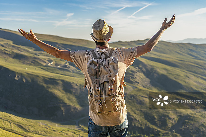 徒步男子在山地景观上背着背包举起双臂的背影图片素材