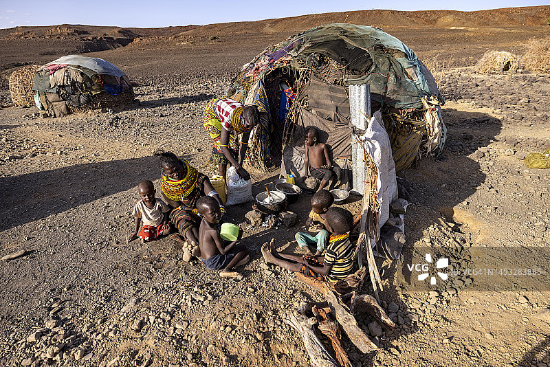 极端贫困、干旱和气候变化导致营养不良的儿童，母亲在住所前准备玉米粥和鱼，肯尼亚图片素材