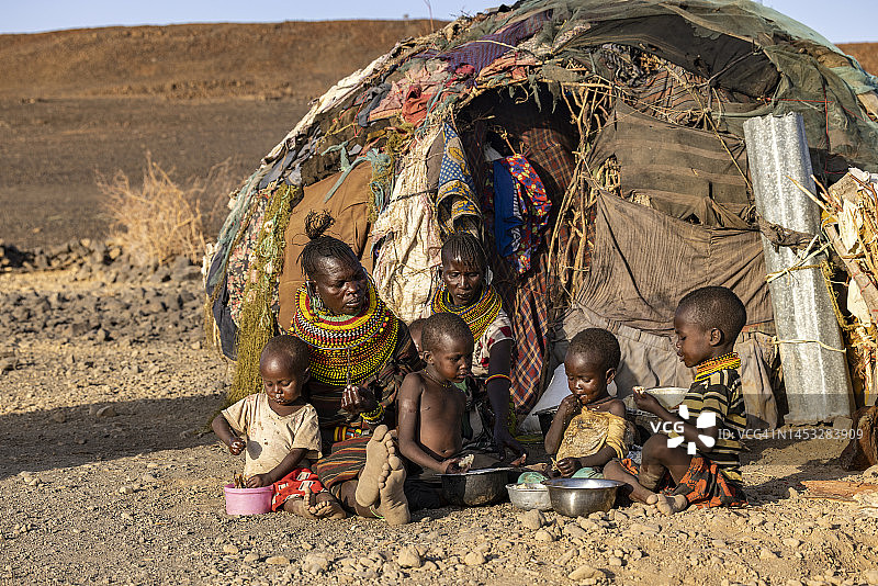 极端贫困、干旱和气候变化导致营养不良的儿童，母亲在住所前准备玉米粥和鱼，肯尼亚图片素材