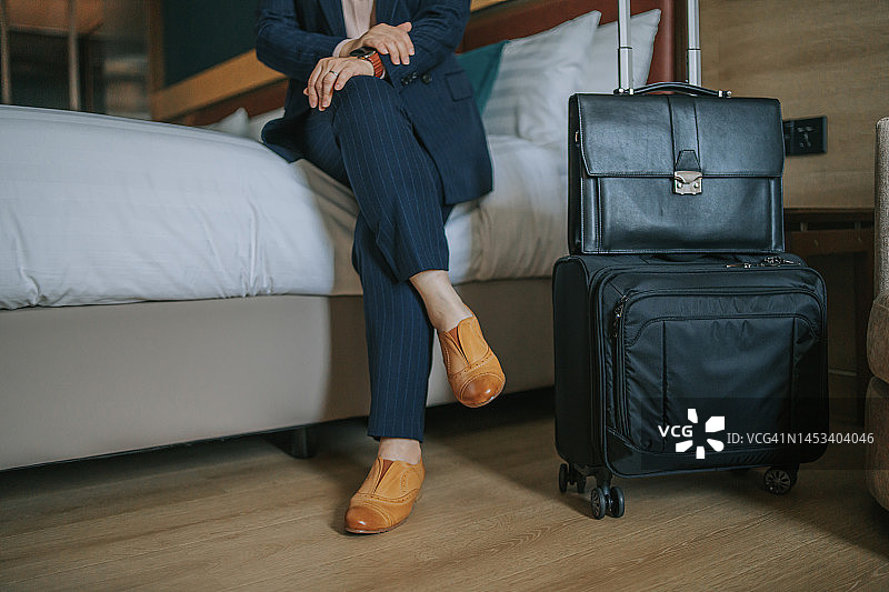 中国女商人坐在床上，旁边放着行李和公文包图片素材