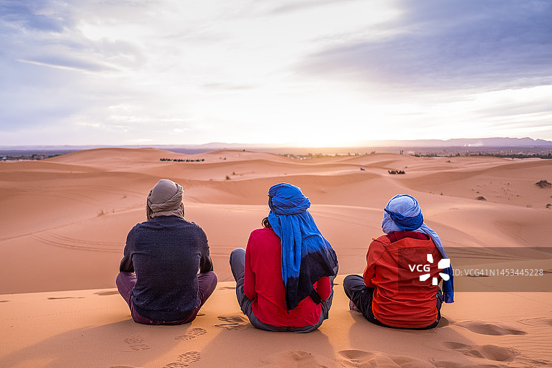 三个旅行者朋友在撒哈拉沙漠的沙丘上观看日落图片素材