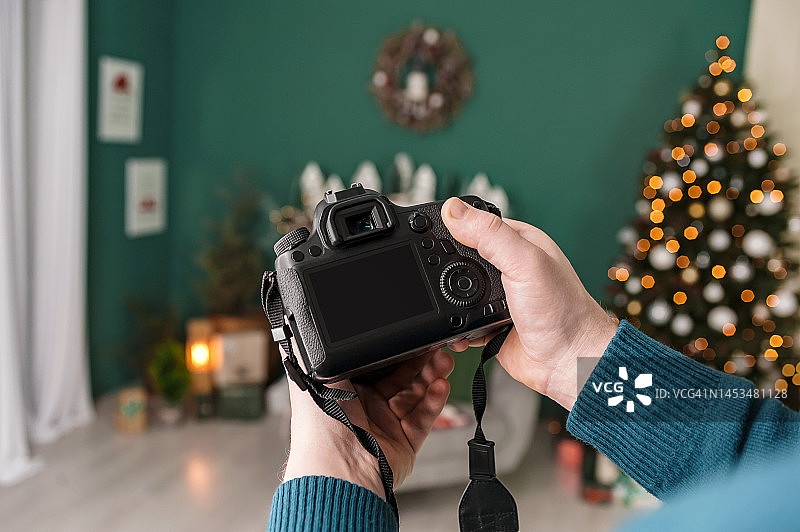 男人手中的专业相机，以圣诞树、装饰品和壁炉为背景图片素材
