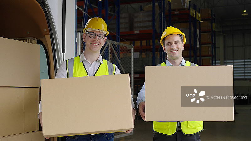 两位微笑的快递员穿着制服，拿着纸板箱看着镜头图片素材