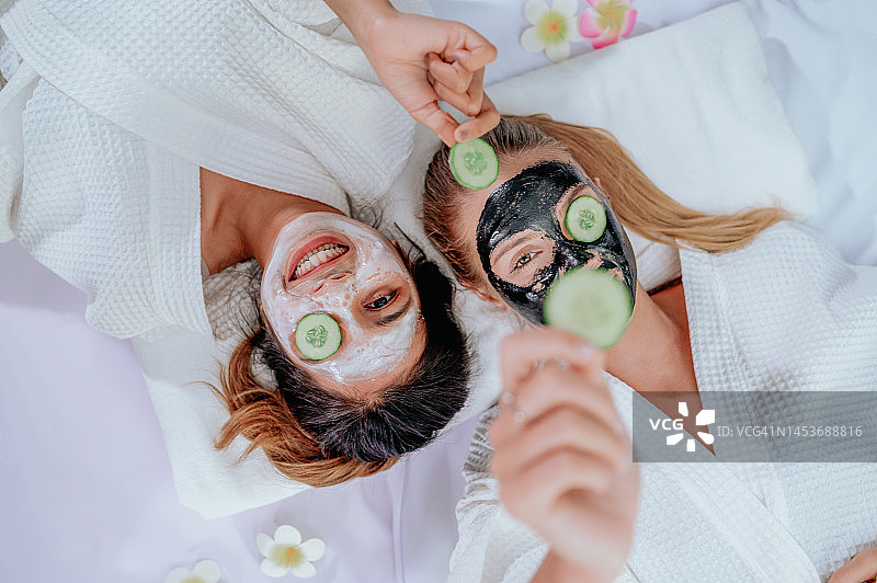 两位快乐的年轻女士一起做黄瓜或番茄面膜图片素材