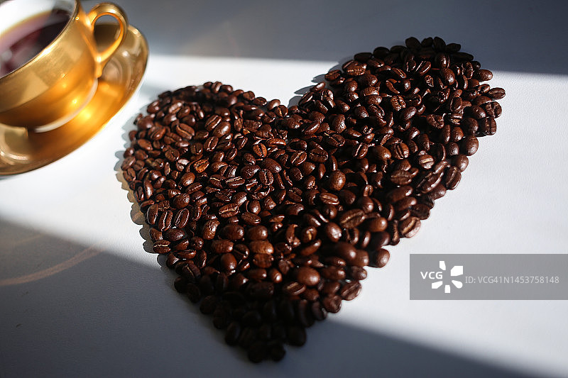 心形烘焙咖啡豆与金色瓷杯背景图片素材