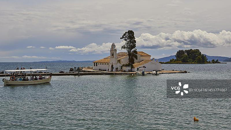 多云天空、载有游客的游览船、修道院建筑、教堂塔楼、高大的树木、科孚岛、希腊爱奥尼亚群岛图片素材