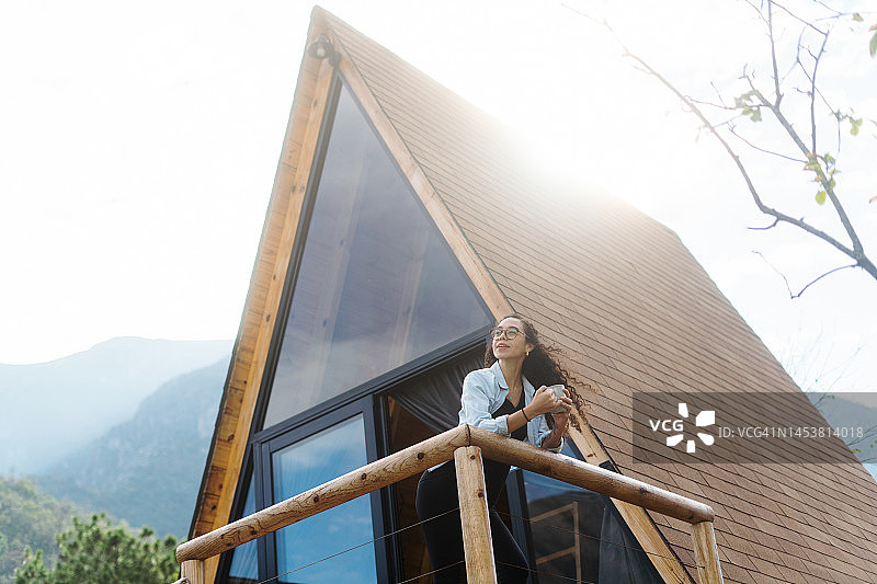 年轻女子站在小木屋外手拿饮料图片素材