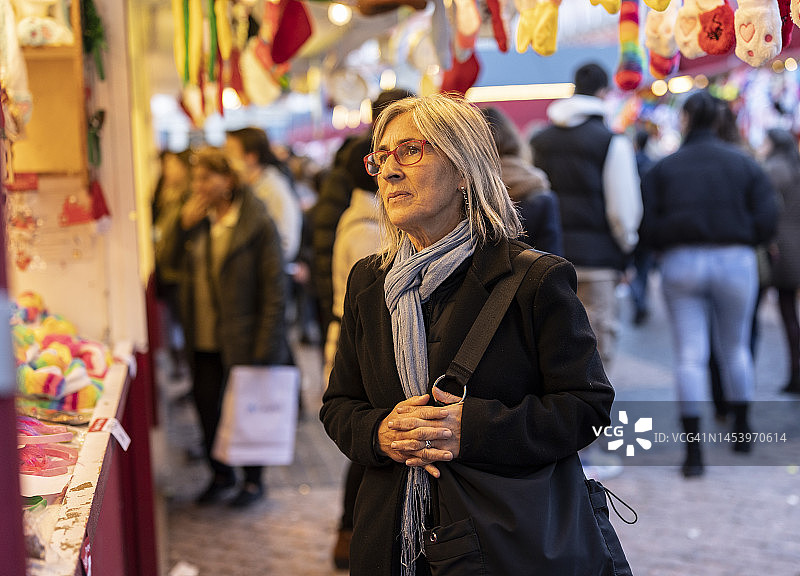 在街边摊购买物品，浏览时表情严肃的灰发中年妇女图片素材