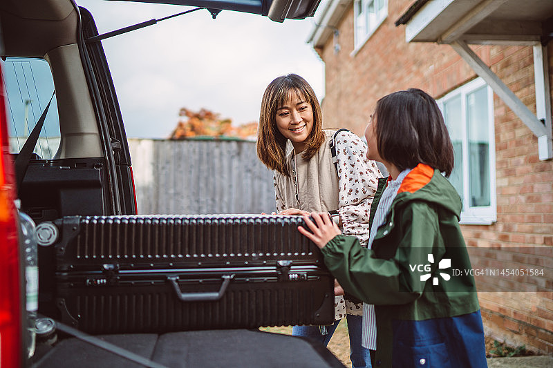 可爱的女孩帮助妈妈将行李装到汽车后备箱里，准备公路旅行图片素材