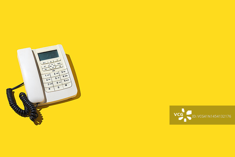 黄色背景左侧的白色复古电话，关于旧式电话、陆线、通话、距离、收听、交换机和客户服务的概念图片素材