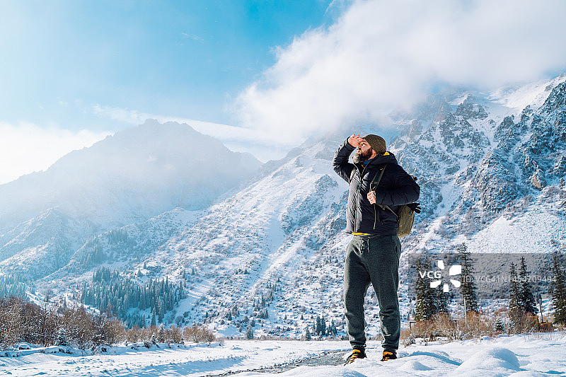 留胡子的背包客身穿保暖的衣服，在冬日山区眺望远方，用手遮住眼睛图片素材