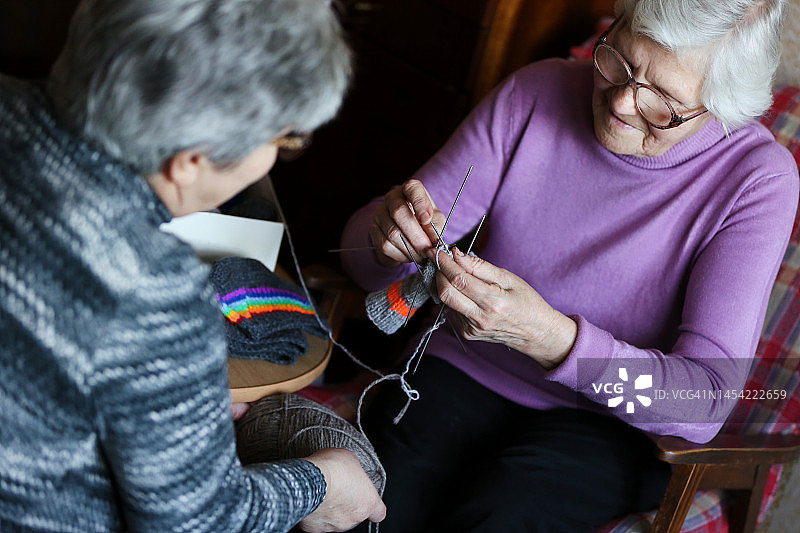 老年妇女编织彩色彩虹袜子，并向女护理员展示她的作品图片素材