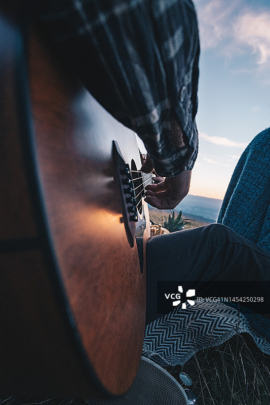 年轻男人在黄昏时在户外弹吉他图片素材