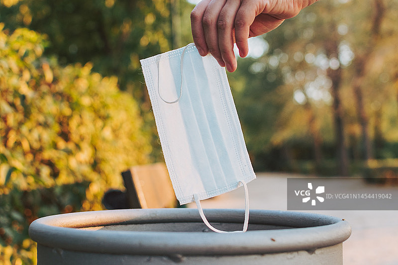一位女士在公园里将医用口罩扔进纸篓图片素材