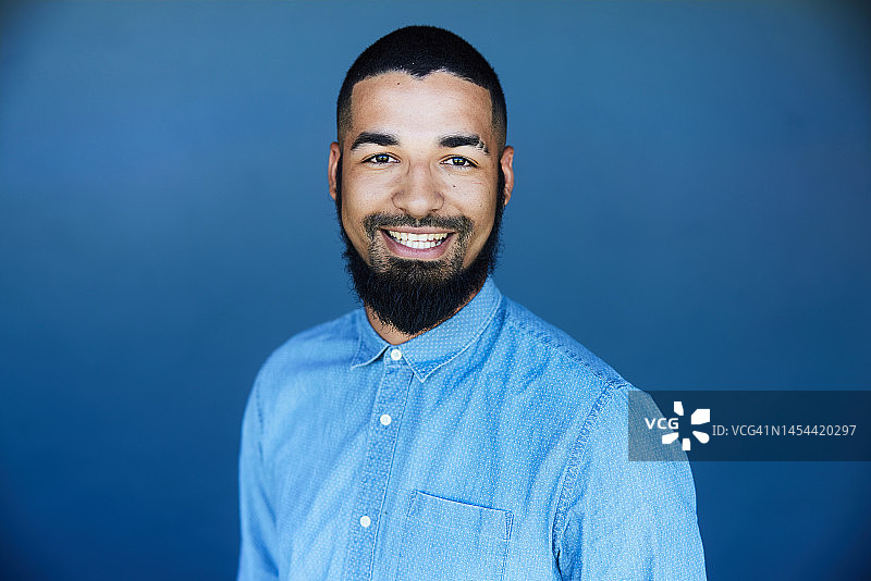 站在蓝色背景前的微笑年轻商人图片素材