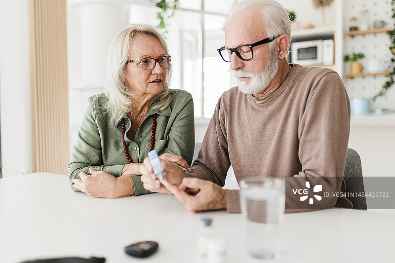 老年夫妇用采血笔在手指上采血，用血糖仪检查血糖，医疗保健，糖尿病，血糖概念图片素材