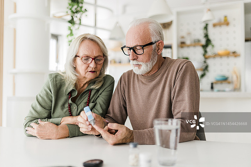 老年夫妇用采血笔在手指上采血，用血糖仪检查血糖，医疗保健，糖尿病，血糖概念图片素材