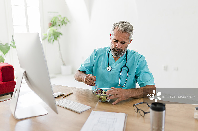 老年医生在办公室工作时吃沙拉图片素材