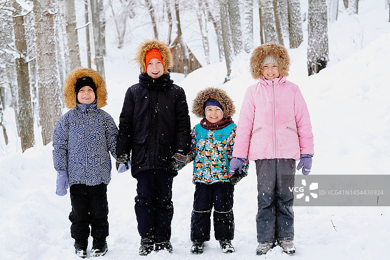 四个孩子在冬日雪林中手牵手徒步旅行图片素材