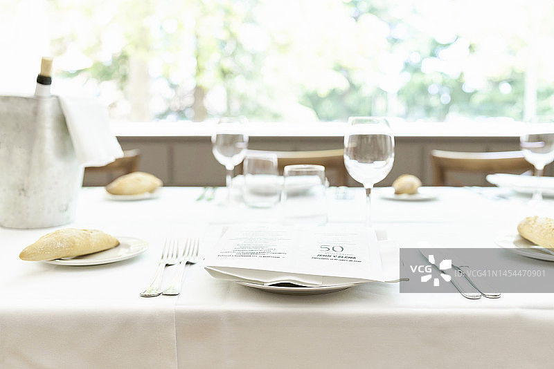 铺着白色桌布的桌子，摆放着盘子、葡萄酒杯、玻璃杯、餐具、香槟和开胃菜图片素材