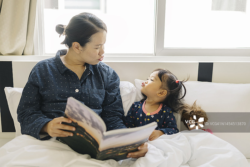 早安，亚洲母亲在床上给女儿讲图画书的故事图片素材